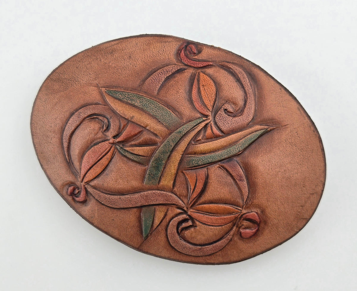 Front of the Hand Tooled Leather Vintage Belt Buckle — Oval Interlaced Vine, showing an oval face with an interlaced vine of tan, green, and rust leaves woven across it.