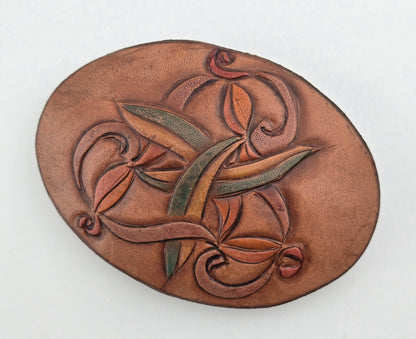 Front of the Hand Tooled Leather Vintage Belt Buckle — Oval Interlaced Vine, showing an oval face with an interlaced vine of tan, green, and rust leaves woven across it.