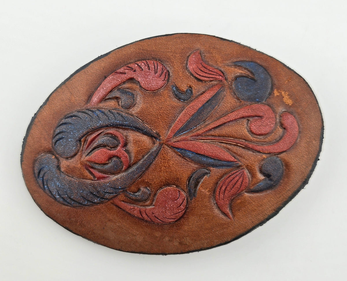 Front of the Hand Tooled Leather Vintage Belt Buckle — Oval Red & Navy Scroll Floral, showing an oval face with swirling red and navy floral scrolls on tan leather.