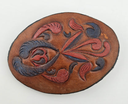 Front of the Hand Tooled Leather Vintage Belt Buckle — Oval Red & Navy Scroll Floral, showing an oval face with swirling red and navy floral scrolls on tan leather.