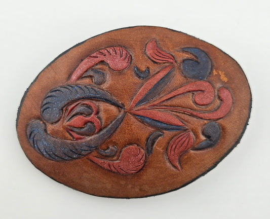 Front of the Hand Tooled Leather Vintage Belt Buckle — Oval Red & Navy Scroll Floral, showing an oval face with swirling red and navy floral scrolls on tan leather.