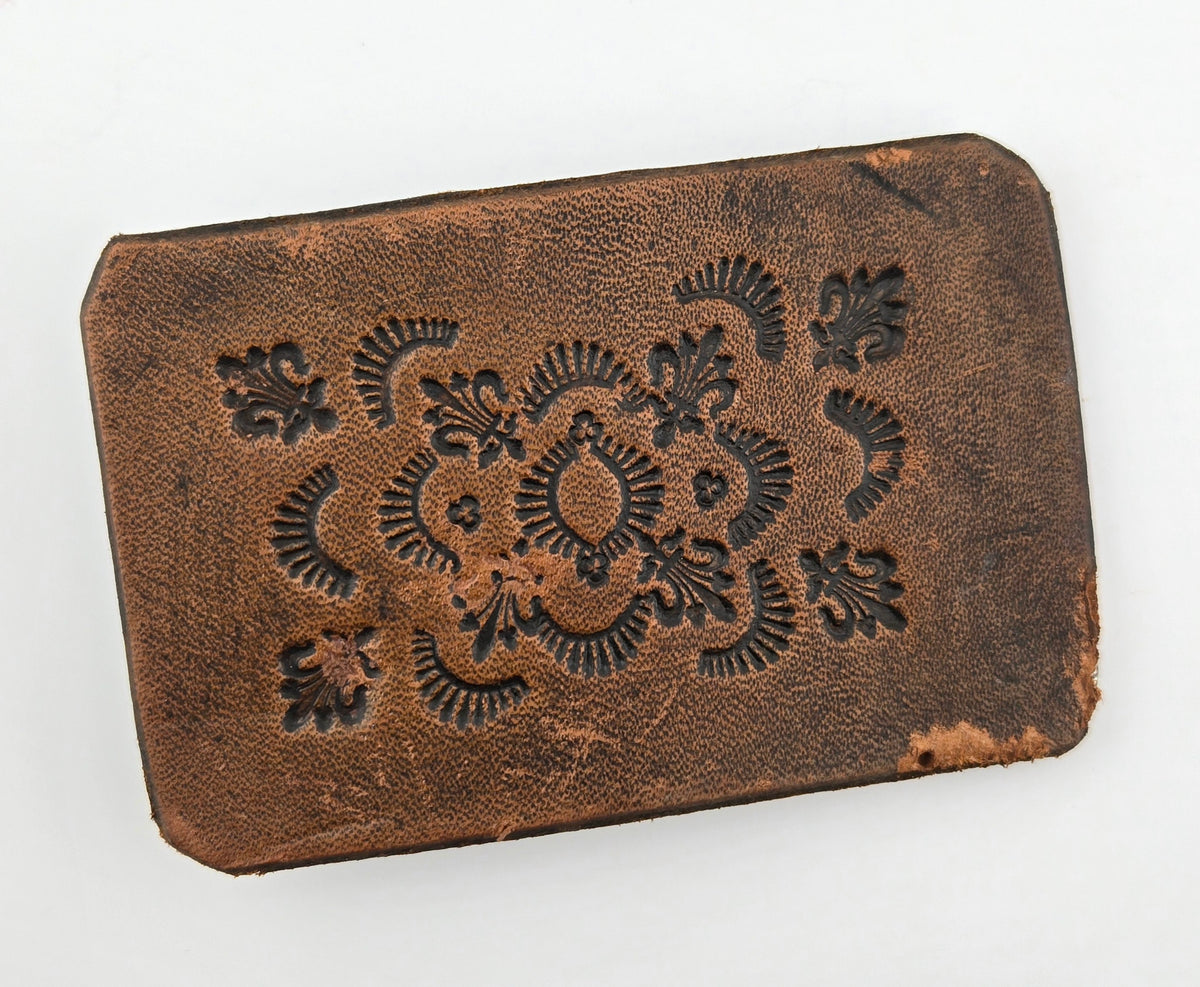 Front of the Hand Tooled Leather Vintage Belt Buckle — Fleur-de-Lis & Sunburst, showing fleur-de-lis stamps ringed by radiating sunburst arcs in dark tooling on a tan-brown face.