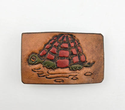 Front of the Hand Tooled Leather Vintage Belt Buckle — Turtle with Red Patchwork Shell, showing a turtle with a bold red patchwork shell and green head and legs on a tan leather face.