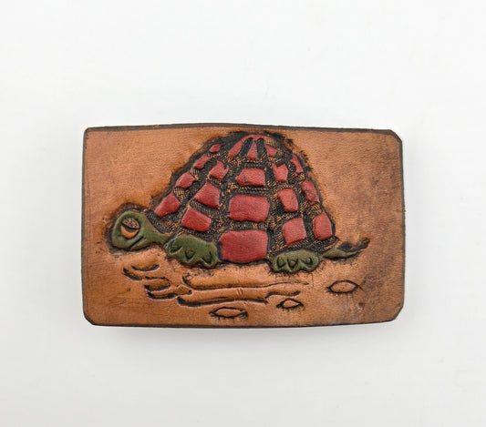 Front of the Hand Tooled Leather Vintage Belt Buckle — Turtle with Red Patchwork Shell, showing a turtle with a bold red patchwork shell and green head and legs on a tan leather face.